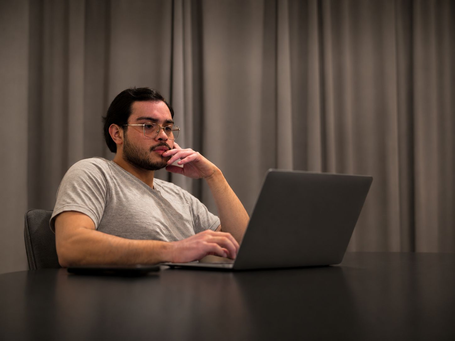 Hombre trabajando con una laptop en un escritorio con luz tenue, en blanco y negro