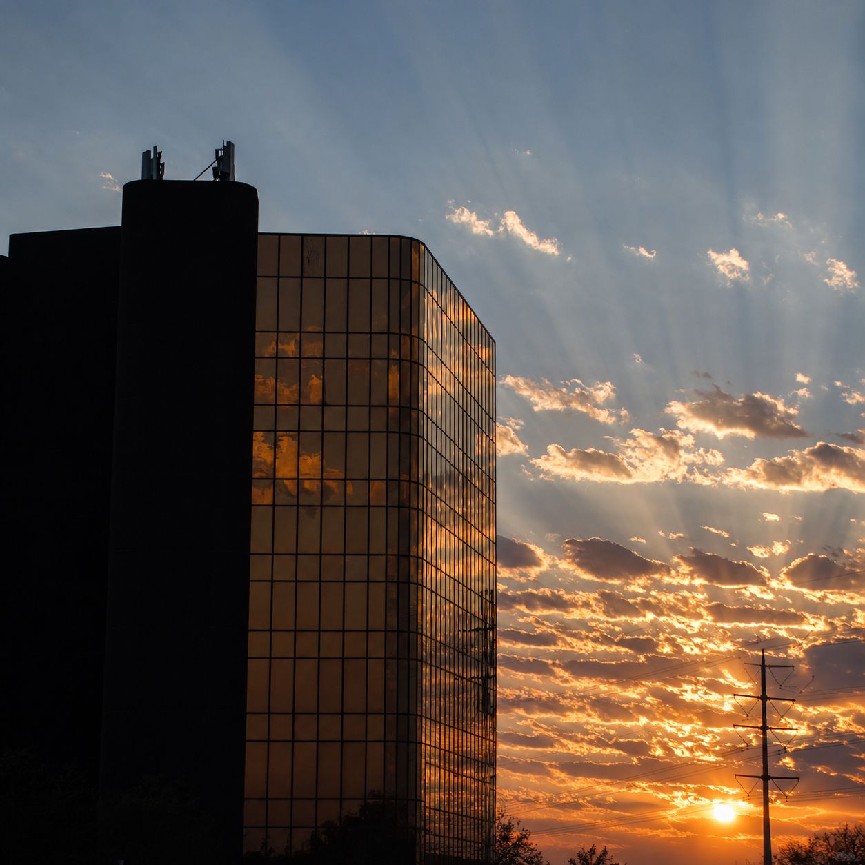 Edificio de vidrio recortado contra un atardecer con rayos de sol entre las nubes