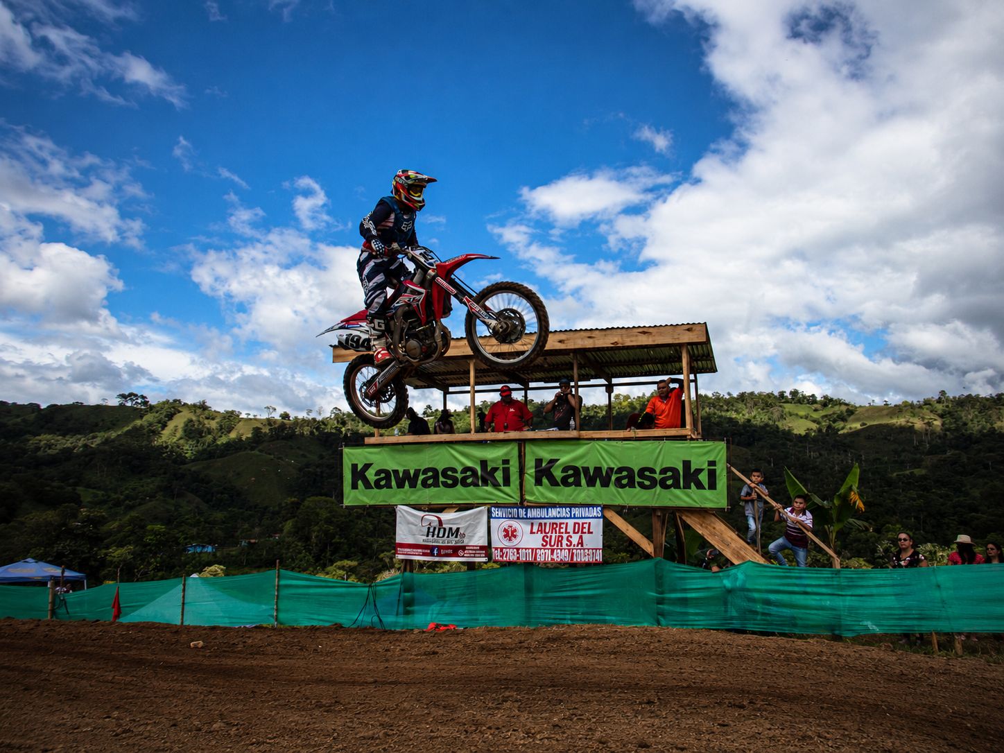 Piloto de motocross saltando desde una rampa de madera contra el cielo azul
